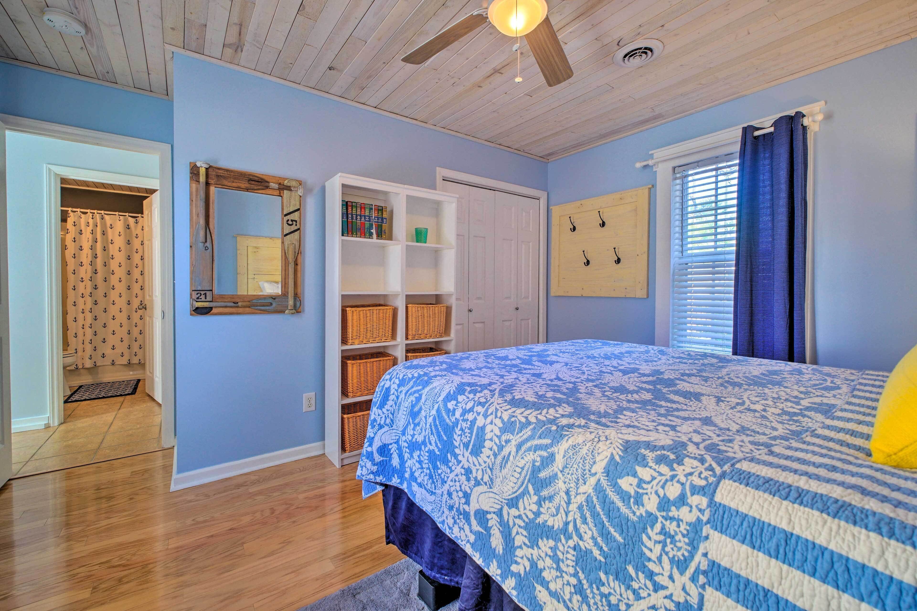 Une chambre avec un plafond en bois, un lit recouvert d’une courtepointe à motifs bleus et blancs, une armoire blanche et un miroir avec un cadre en bois.