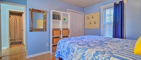 Une chambre avec un plafond en bois, un lit recouvert d’une courtepointe à motifs bleus et blancs, une armoire blanche et un miroir avec un cadre en bois.