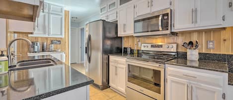 A modern kitchen with white cabinets, stainless steel appliances, a granite countertop, and a wooden backsplash.