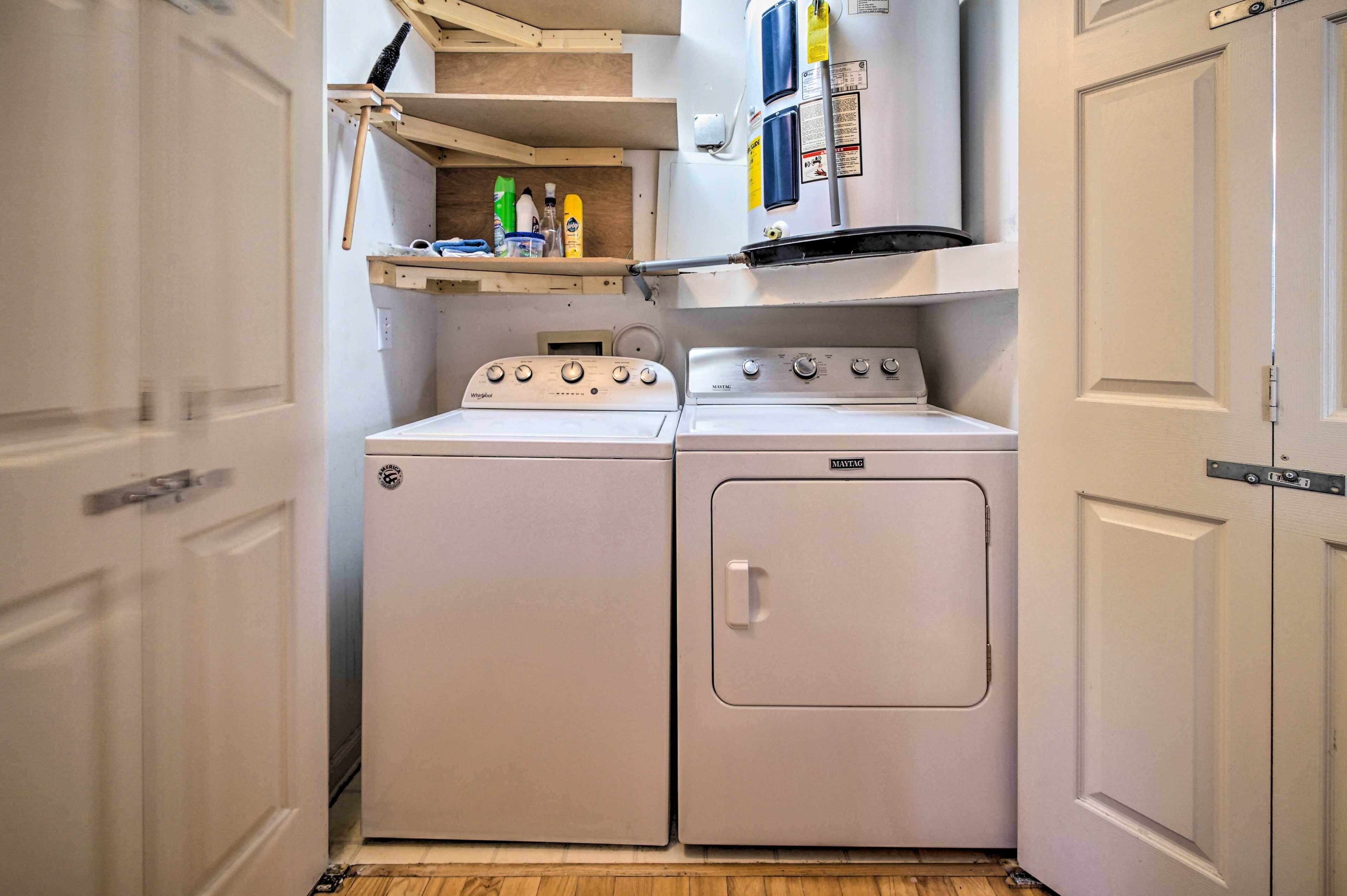 Une petite buanderie comprenant deux machines à laver blanches et un sèche-linge, une étagère avec des produits de nettoyage et une porte blanche.