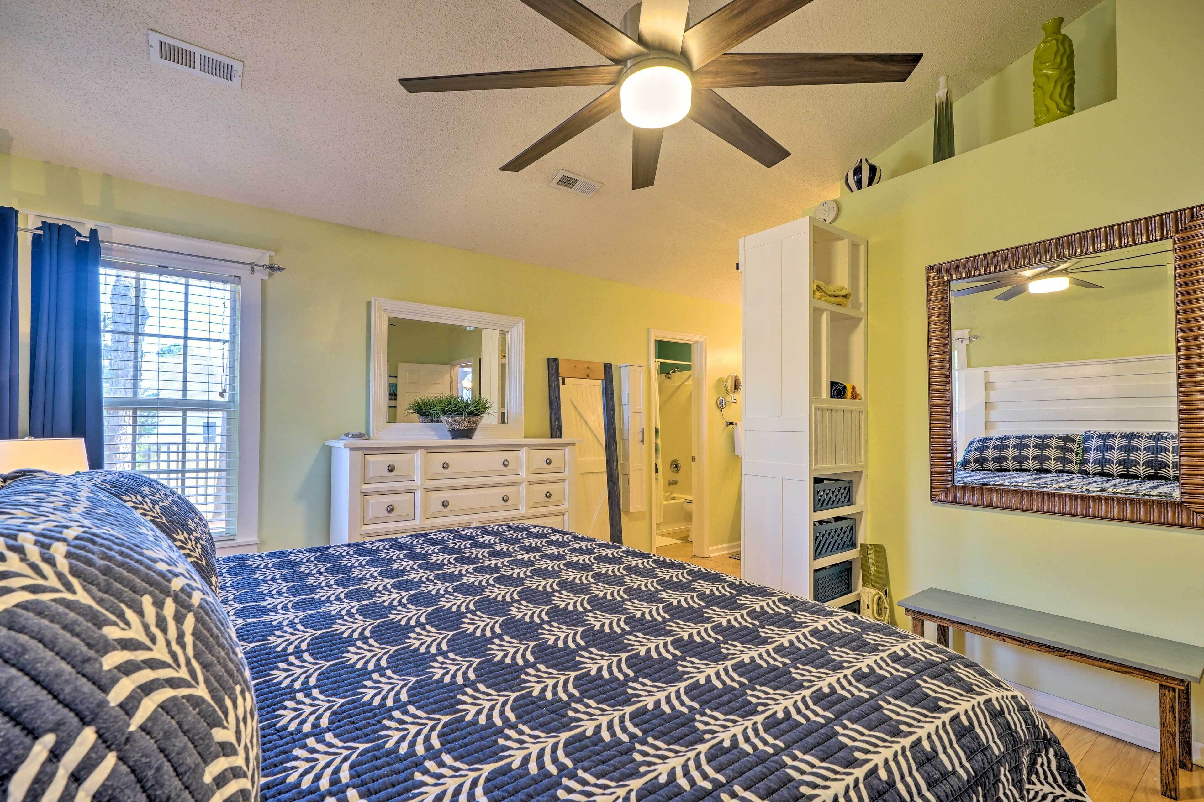 A bedroom with a bed, a dresser, a mirror, and a ceiling fan.