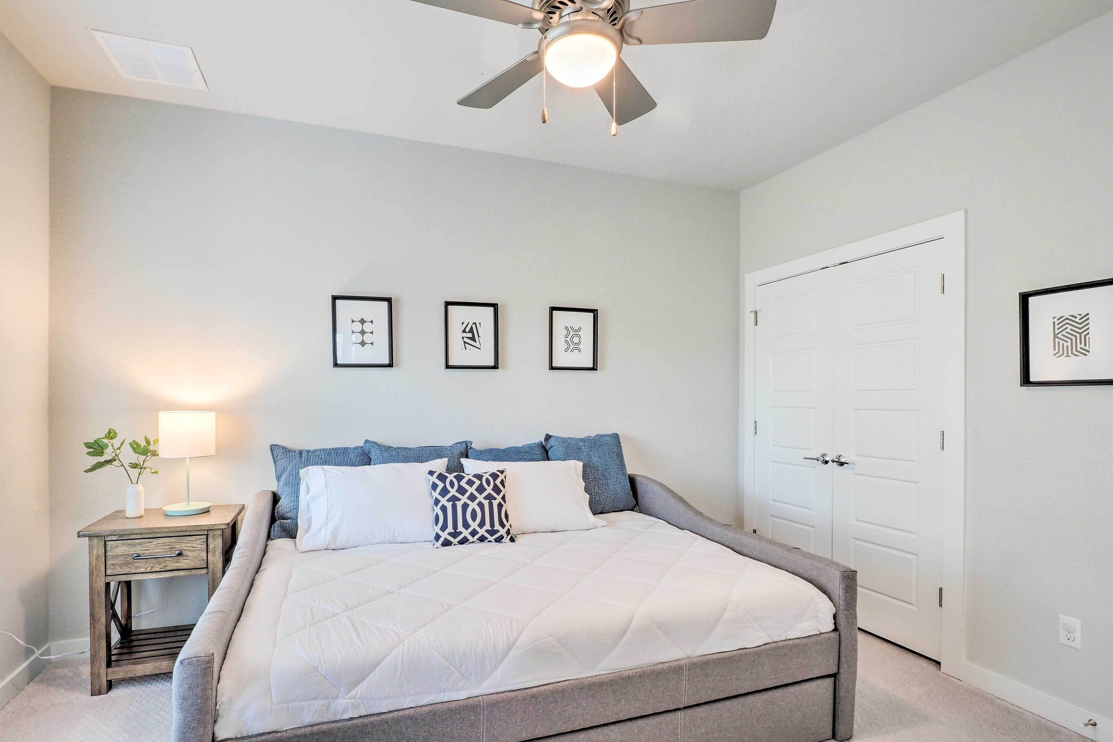 A bedroom with a bed, a nightstand, a ceiling fan, and a door.