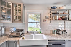 A kitchen with a large window, a dish rack, a coffee maker, and a shelf with pots and pans.