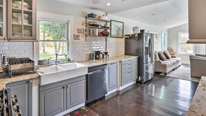 A modern kitchen with grey cabinets, stainless steel appliances, and a large window offering a view of the outdoors.
