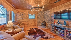 A cozy living room with a wooden ceiling, a large flat-screen TV, leather sofas, a cowhide rug, and a fireplace. - 2 Mi to Choctaw Landing: 'western Daze' Cabin! (Broken Bow)