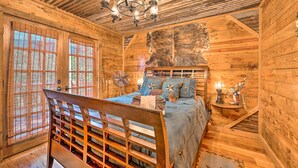 A wooden cabin bedroom with a bed, a wooden headboard, a chandelier, and a fan. - 2 Mi to Choctaw Landing: 'western Daze' Cabin! (Broken Bow)