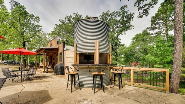 A rustic outdoor patio with a cylindrical metal structure, wooden deck, and metal chairs. - 2 Mi to Choctaw Landing: 'western Daze' Cabin! (Broken Bow)