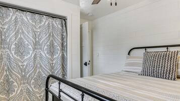 A bedroom with a bed, a patterned curtain, a ceiling fan, and a door leading to another room.
