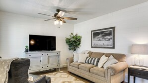 A living room with a television, a sofa, a coffee table, a ceiling fan, a framed picture, and a lamp. - Cozy Farmhouse-style Cottage by Mighty 5 Ntl Parks (Circleville)
