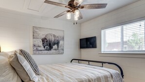 A bedroom with a bed, a ceiling fan, a mounted TV, and a window with blinds. - Cozy Farmhouse-style Cottage by Mighty 5 Ntl Parks (Circleville)