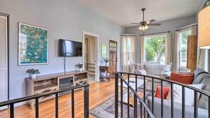 A spacious living room with a wooden floor, a black TV, a ceiling fan, and a large window with curtains. - Charming Santa Paula Home - Walk to Downtown! (Santa Paula)