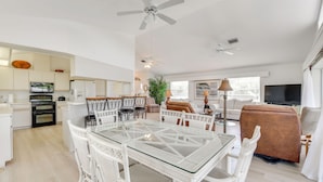 A spacious living area with a glass-top dining table surrounded by white wicker chairs, a brown sofa, and a television. - Canalfront Home w/ Private Dock - 5 Mi to Beaches! (Englewood)