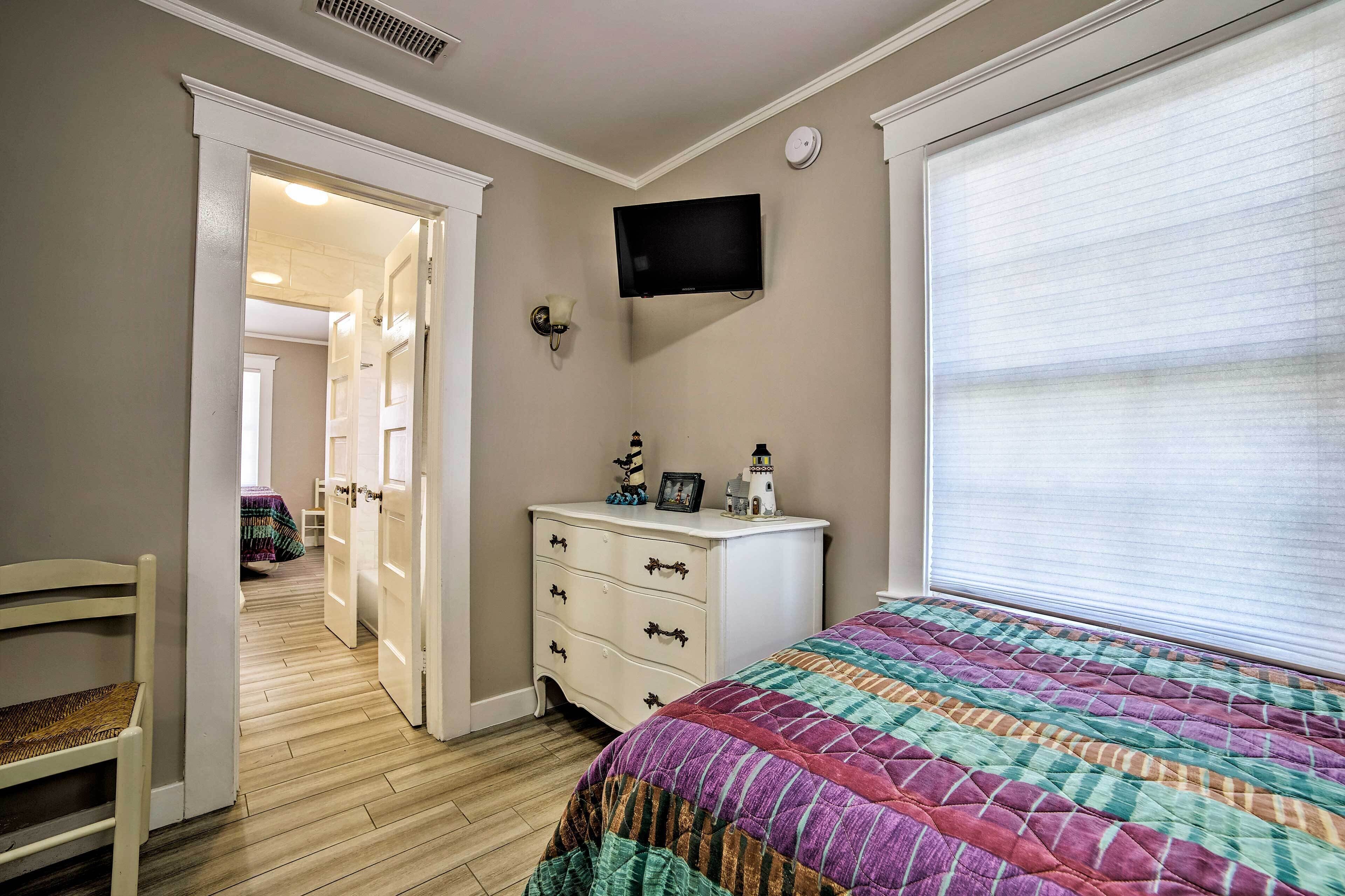 A bedroom with a bed, a dresser, a television, and a window with blinds.