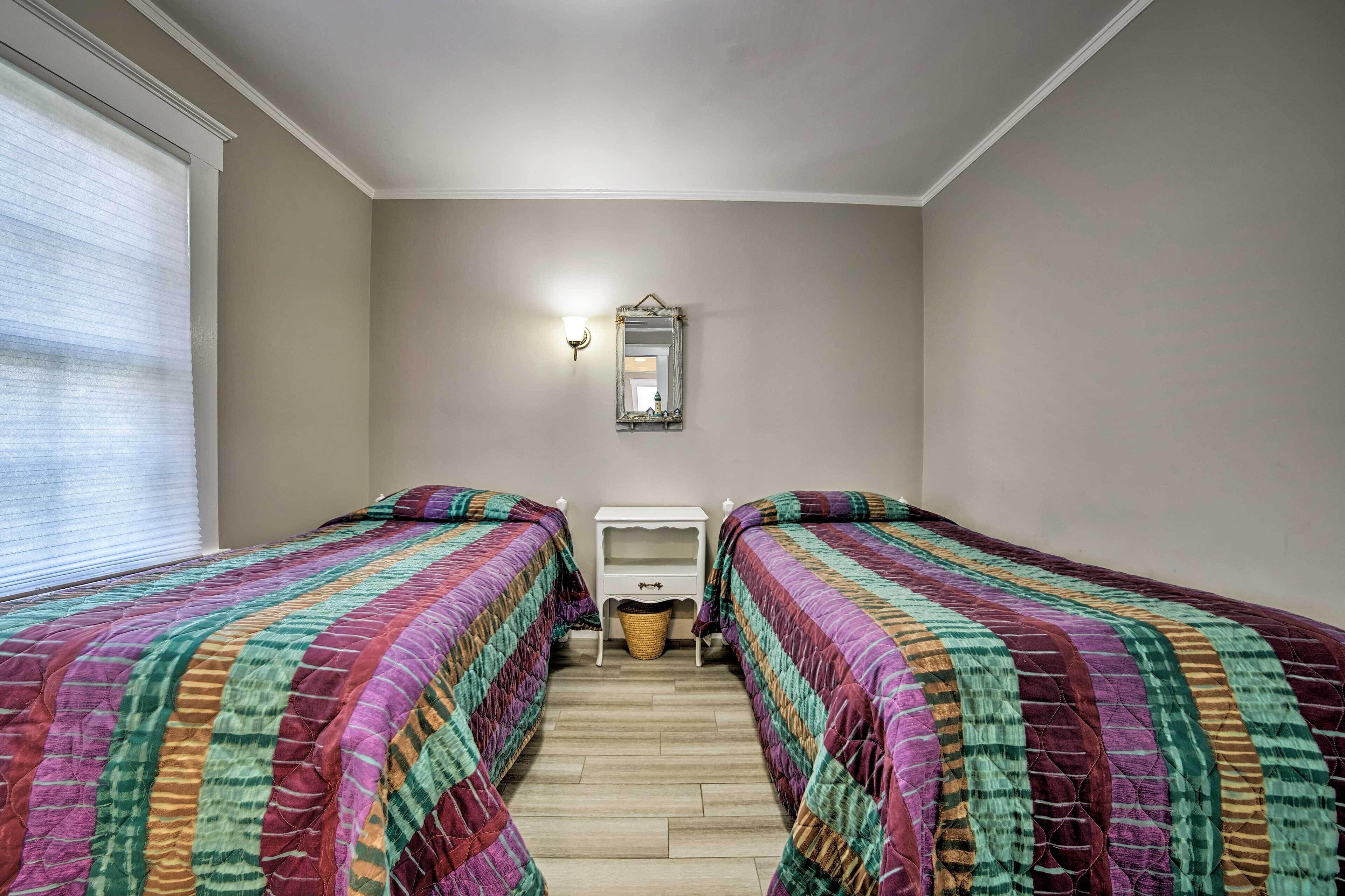Un dormitorio con dos camas, una mesita de noche pequeña, un espejo y una ventana con persianas.