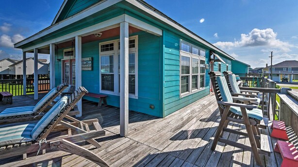 A turquoise beach house with a wooden deck, lounge chairs, and a covered porch.