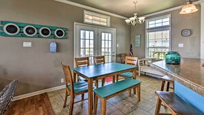 A dining area with a wooden table and chairs, a chandelier, and a kitchen counter with a green vase.