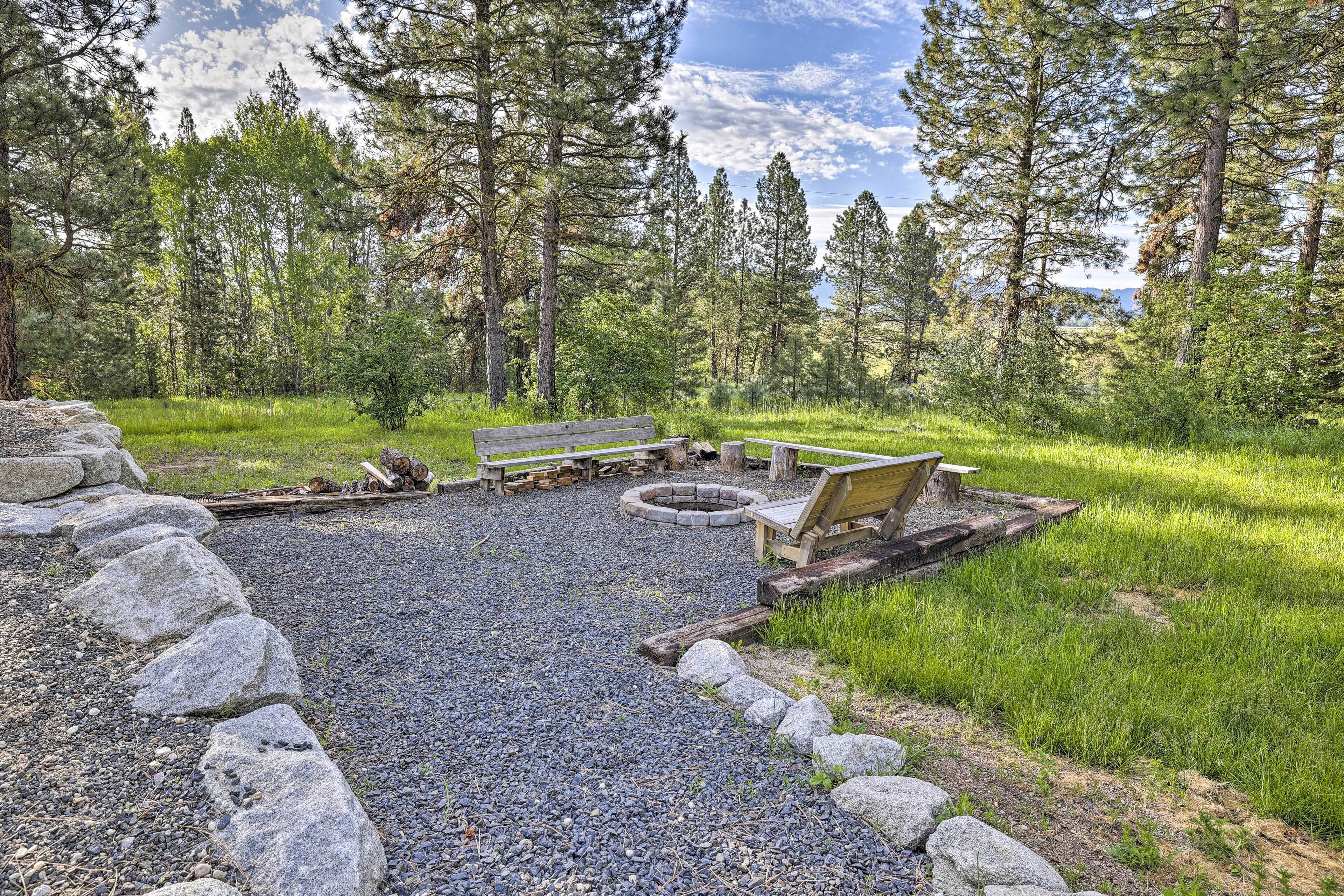 A campground with a fire pit, picnic tables, and a bench.