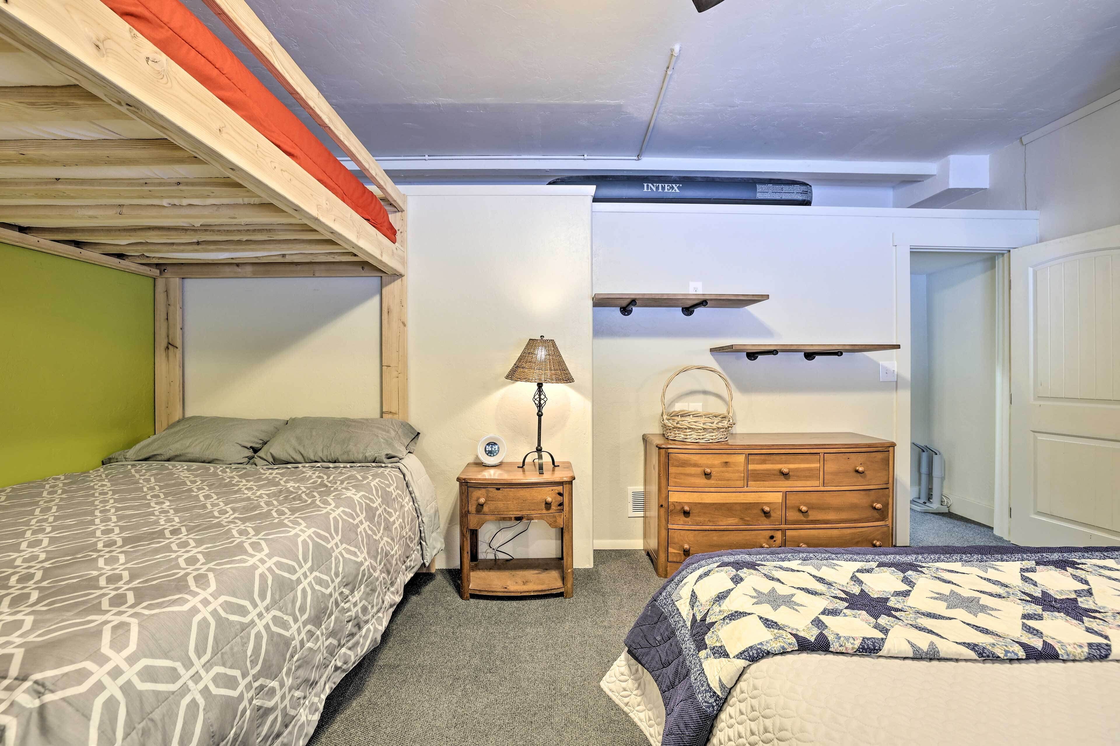 Une chambre avec deux lits, une table de chevet avec une lampe, une commode en bois et un ventilateur de plafond.