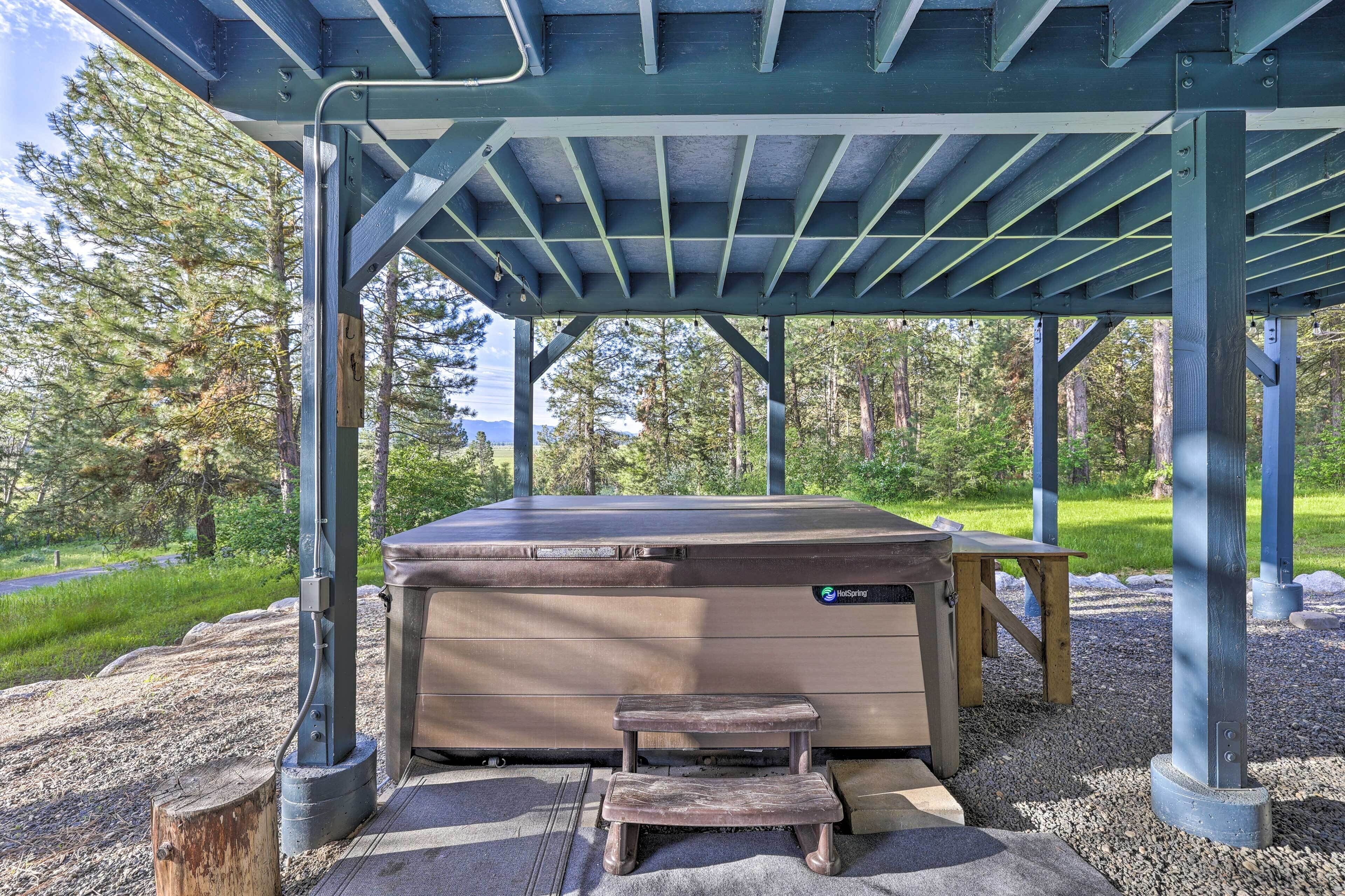 A hot tub under a covered area with a wooden bench and a small stool.
