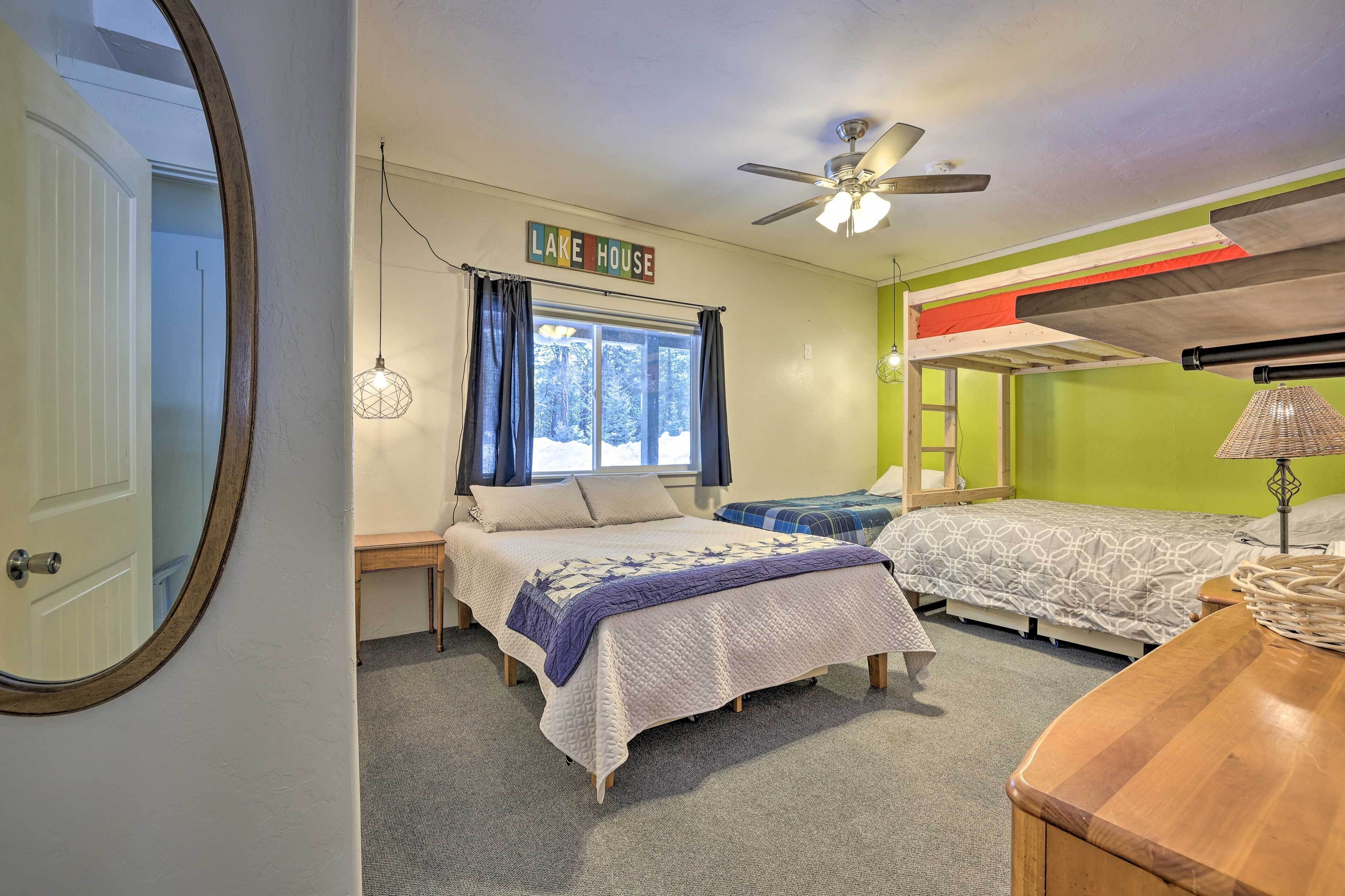 Une chambre avec deux lits, un ventilateur de plafond, une fenêtre avec des rideaux et une pancarte sur laquelle on peut lire « MAISON AU BORD DU LAC ».