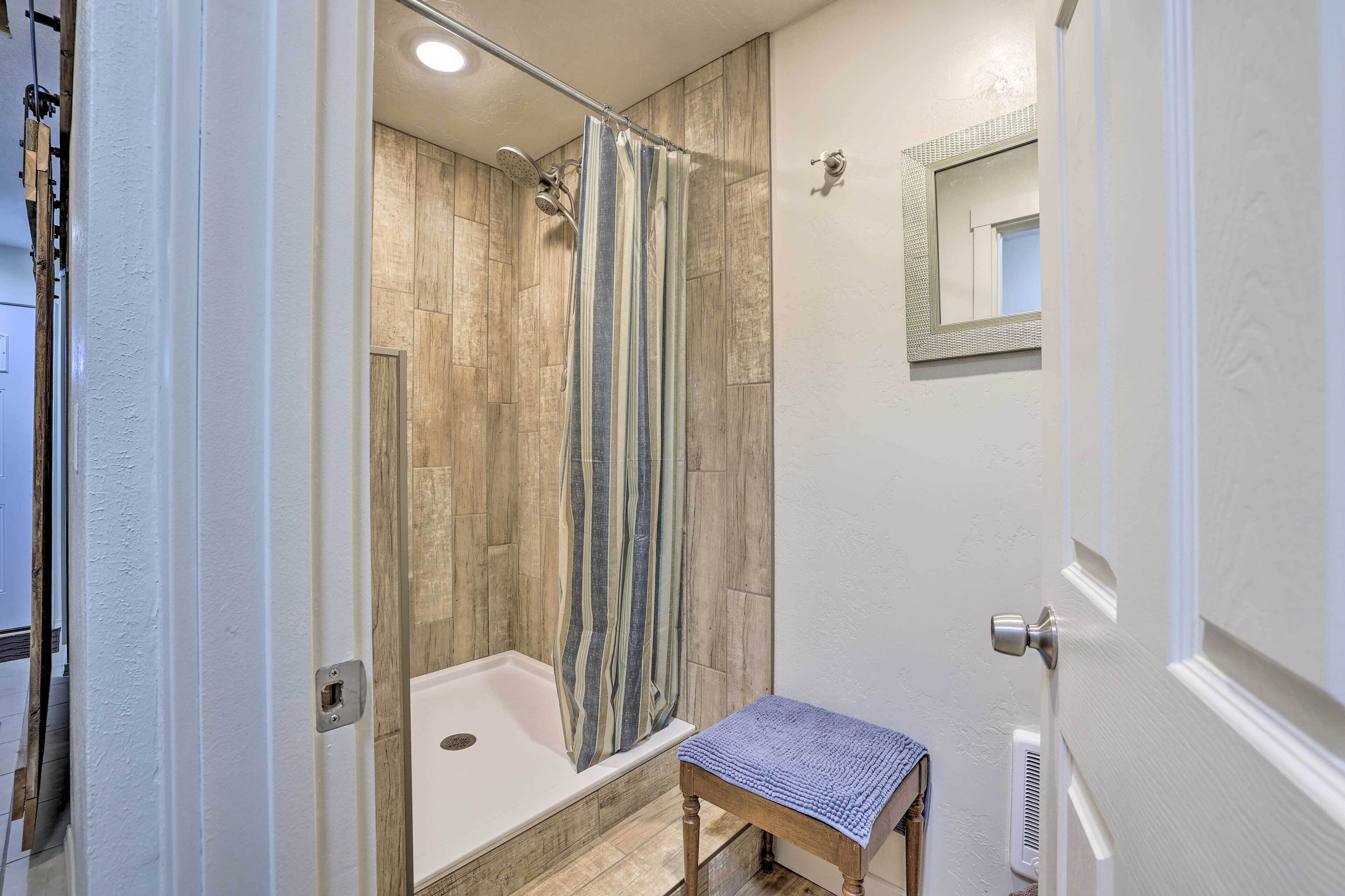 A bathroom with a shower, a bathtub, a wooden floor, a towel rack, and a mirror on the wall.