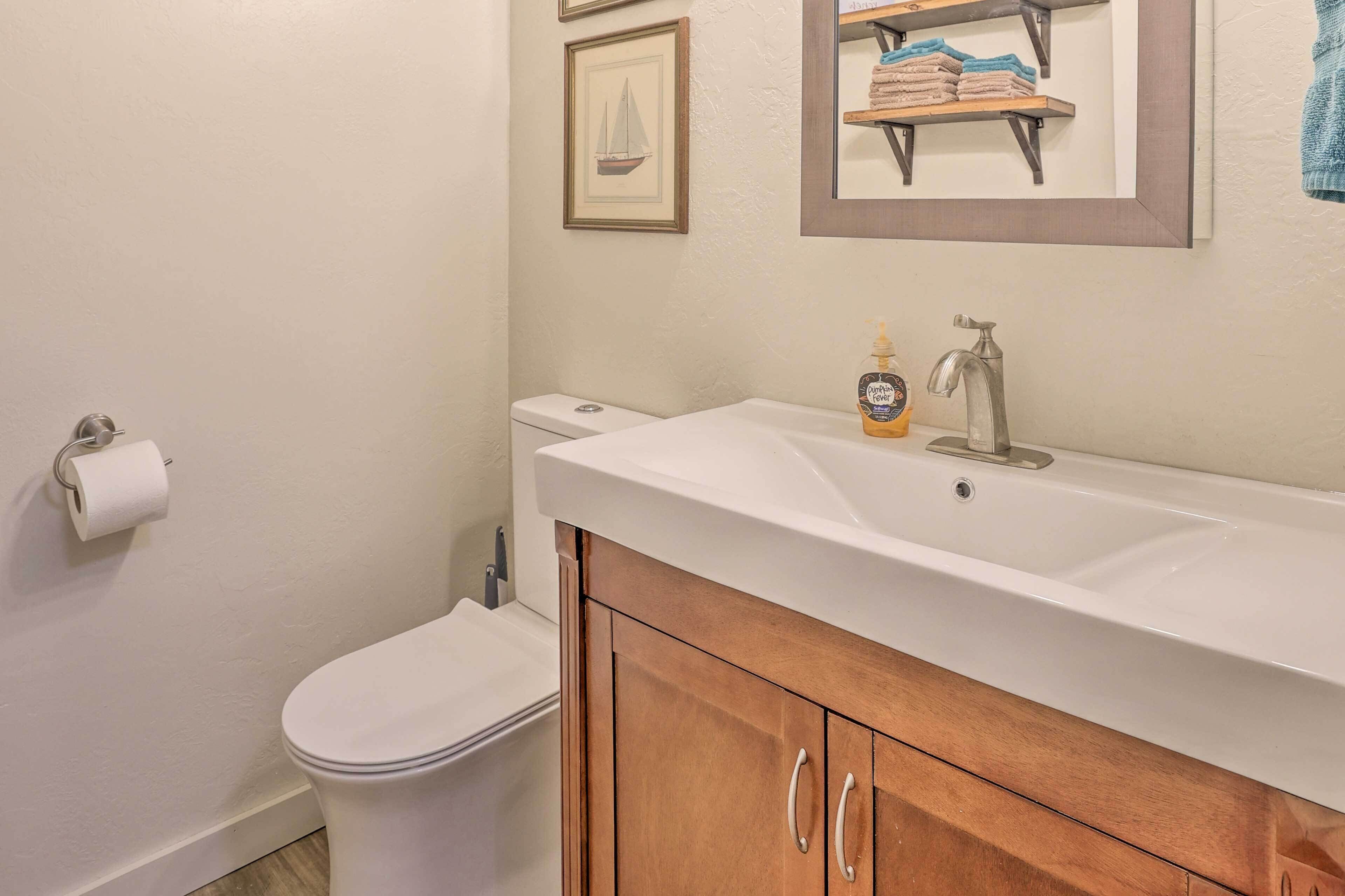 Une salle de bain avec des toilettes blanches, un meuble en bois avec un lavabo et, au mur, un tableau représentant un voilier.