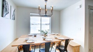 Un coin repas avec une grande table en bois, des chaises noires et un lustre moderne. Une grande fenêtre offre une vue sur un paysage enneigé.