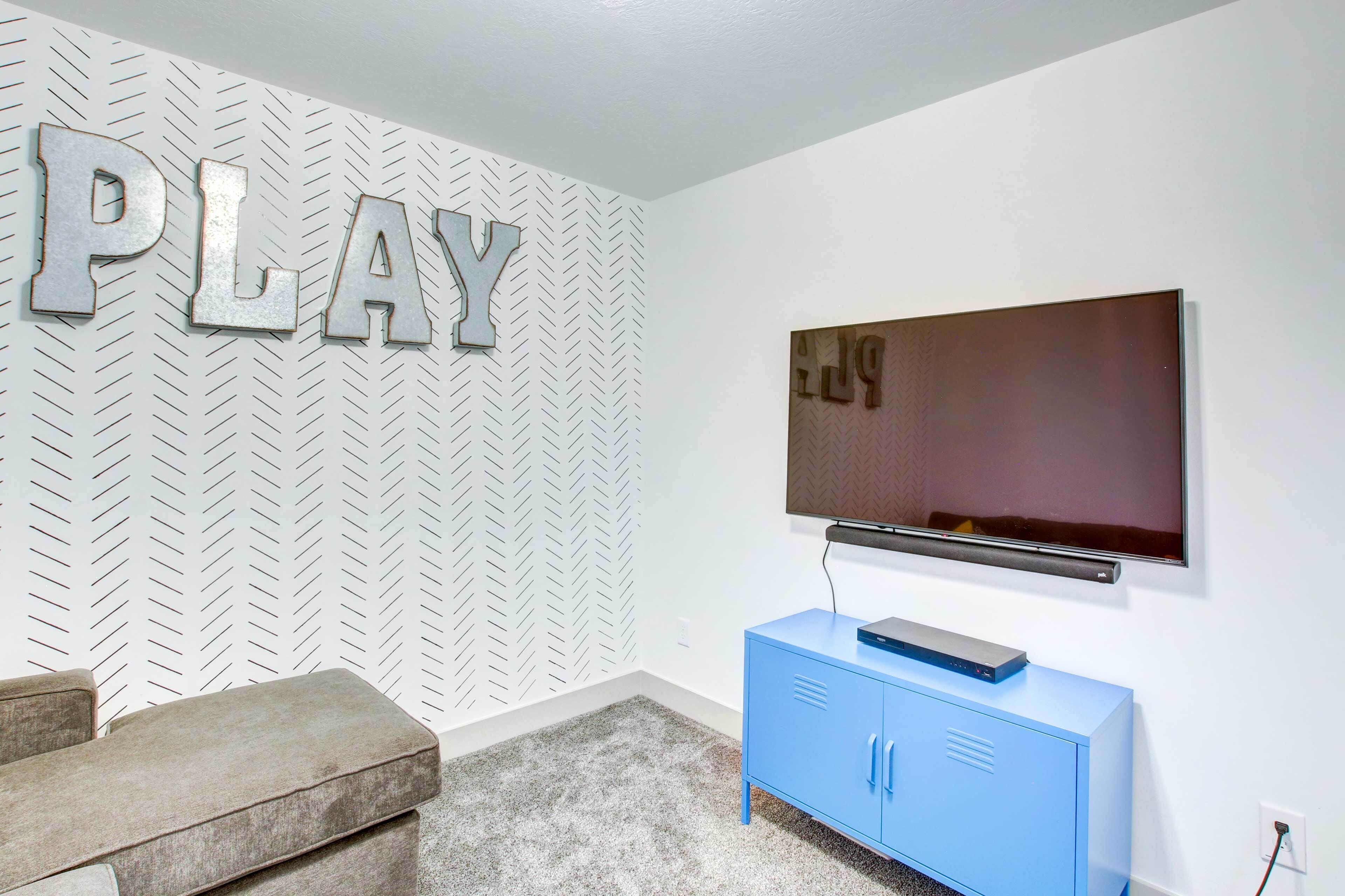 Una habitación con una pared de patrón espiga, un televisor de pantalla plana sobre un mueble azul y un sofá gris.
