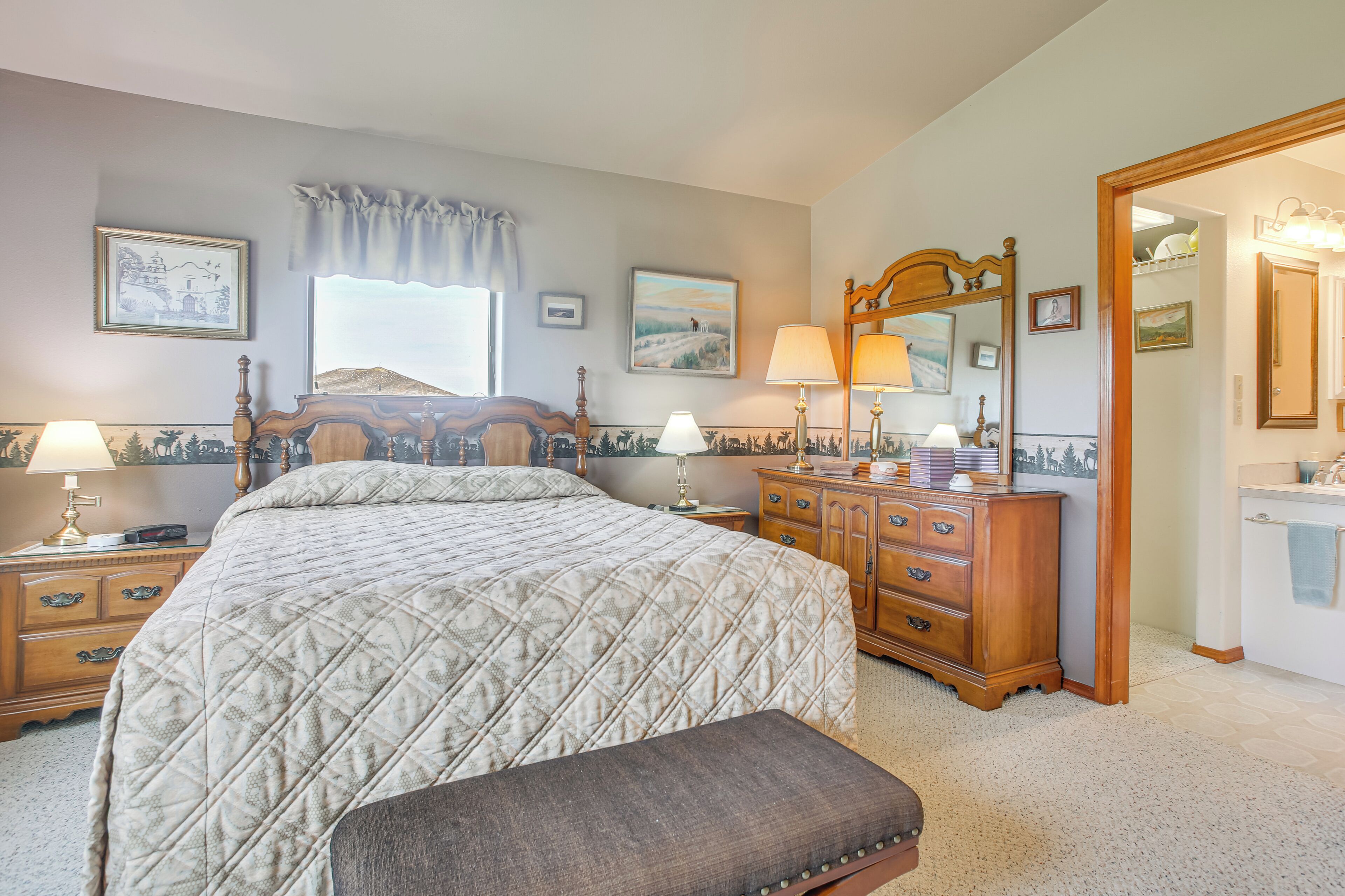 A bedroom with a large bed, a dresser, a mirror, and a window with a view.