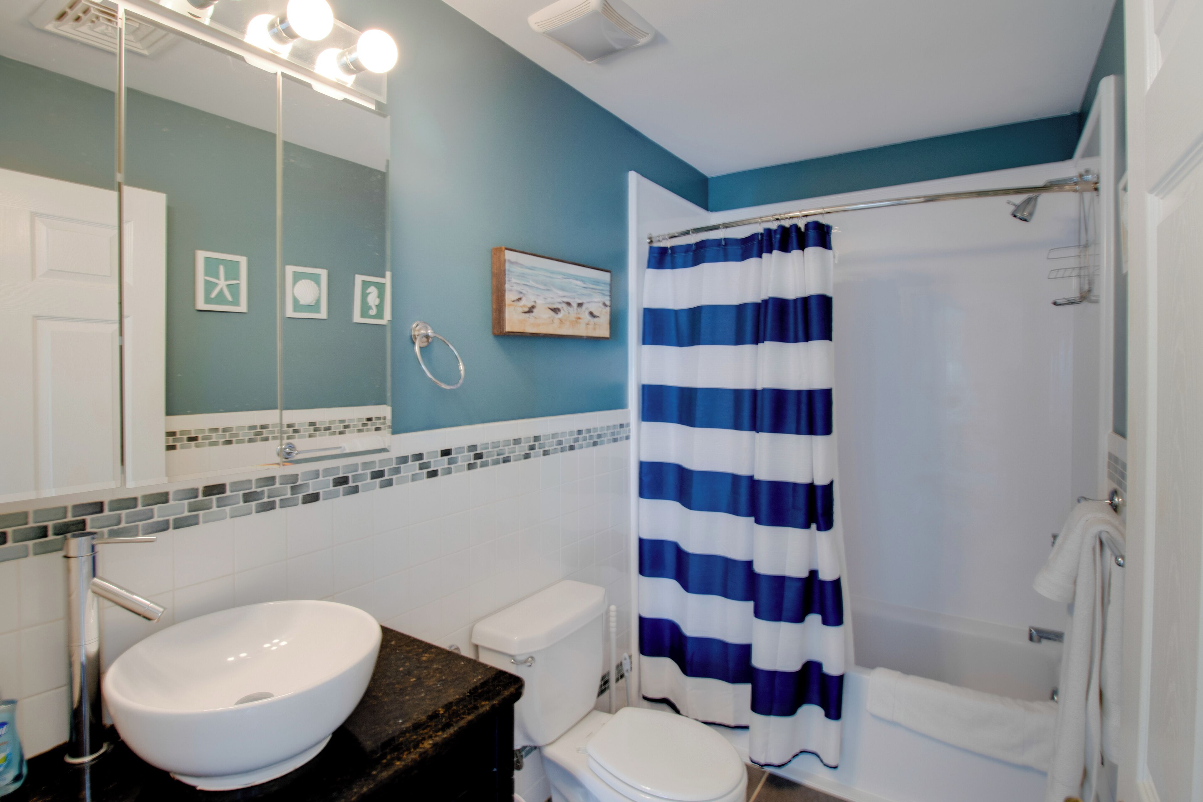 A bathroom with a white sink, toilet, and bathtub. There is a blue and white striped shower curtain.