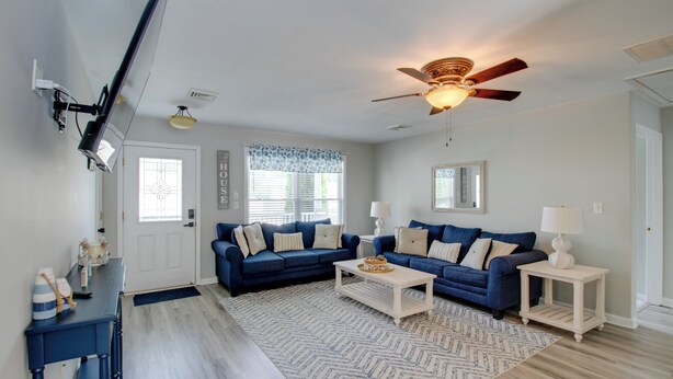 A living room with two blue sofas, a white coffee table, a ceiling fan, and a patterned rug. - Charming Somers Point House w/ Private Pool! (Somers Point)
