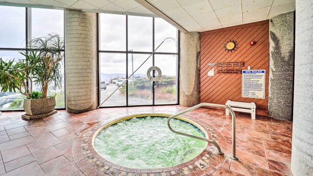 Ett spaområde med ett bubbelbad, stora fönster och en väggpanel av trä med en klocka.