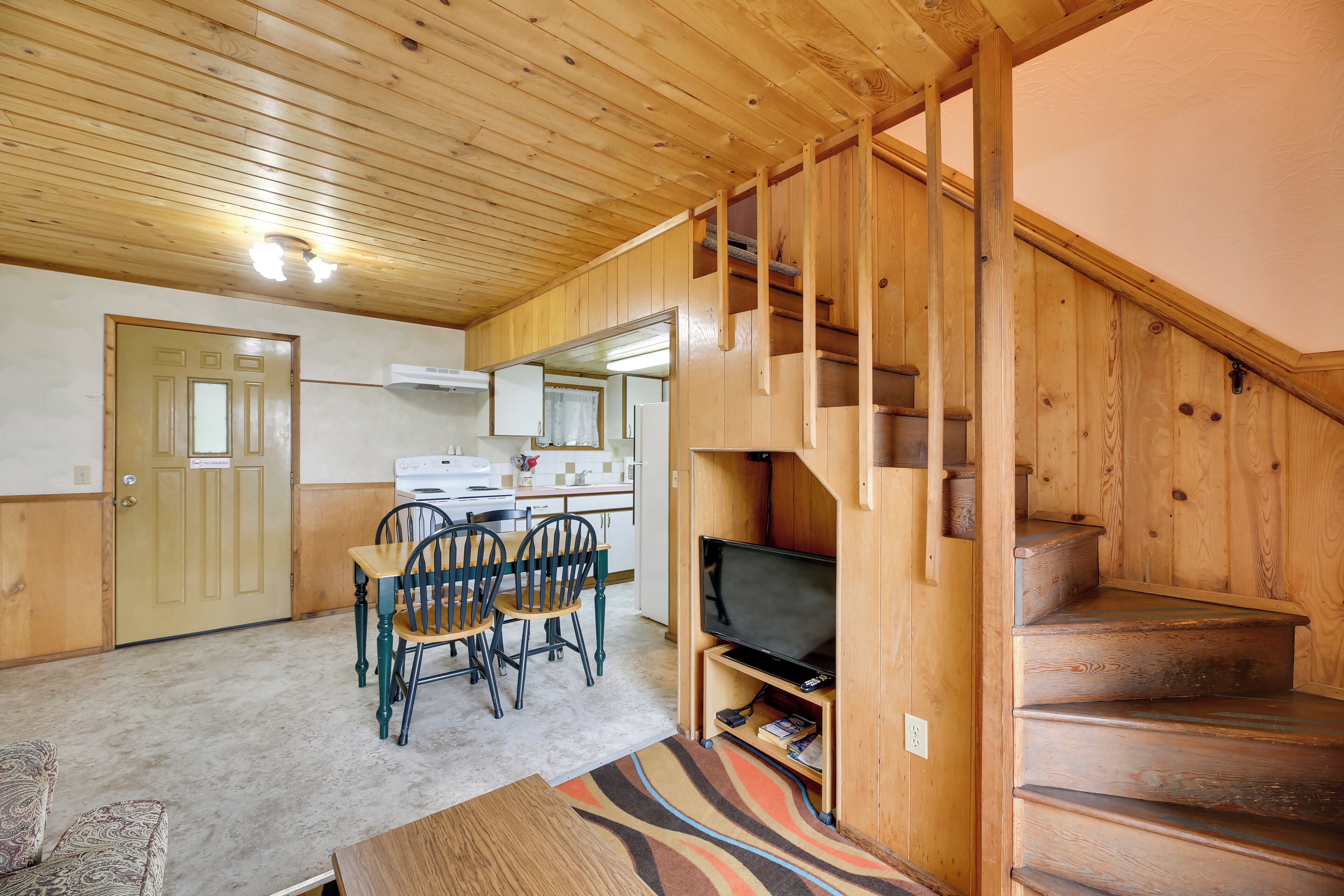 A wooden interior with a dining area, a television, and a staircase.