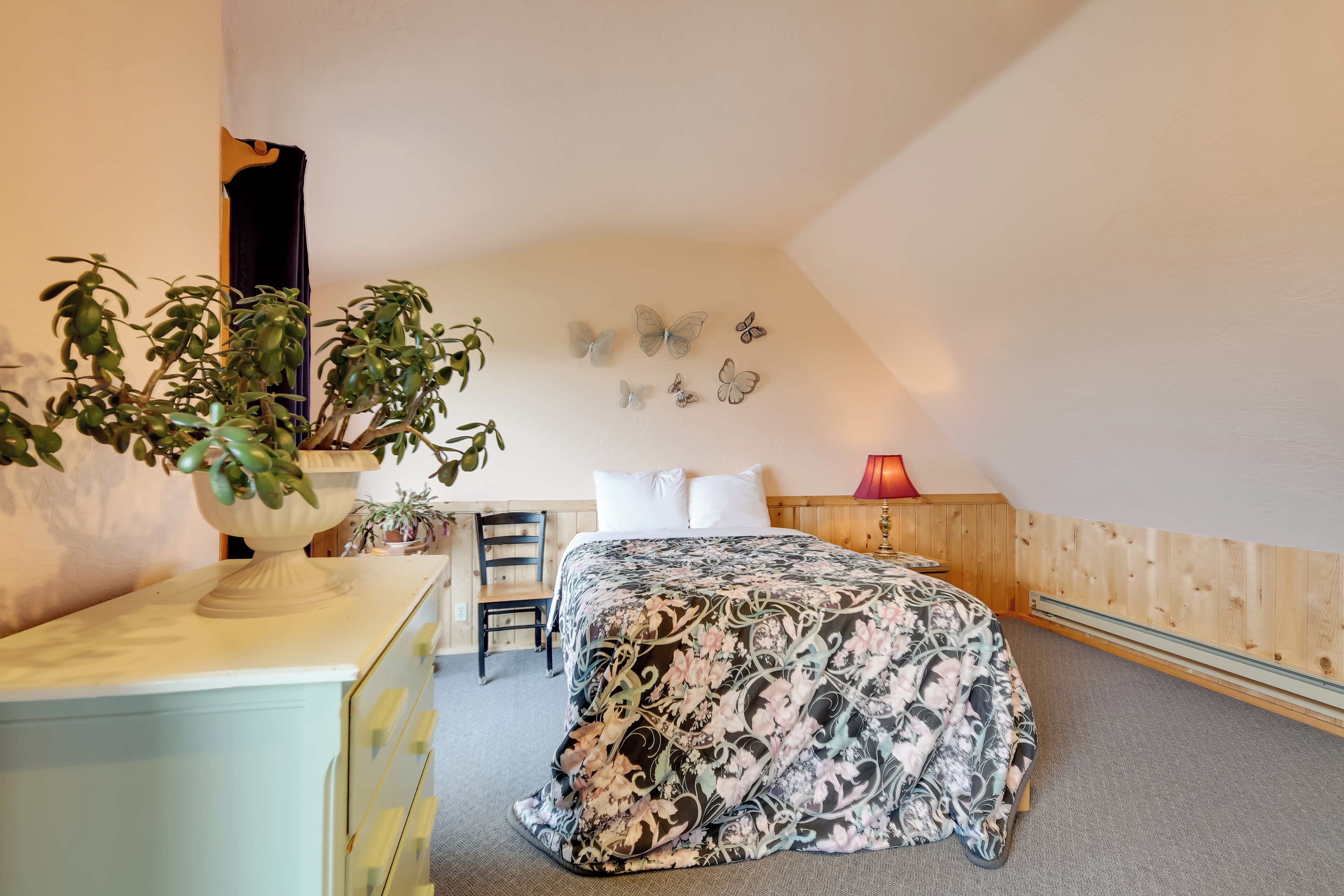 Un dormitorio con cama, cómoda, silla, planta en maceta y adornos en la pared.