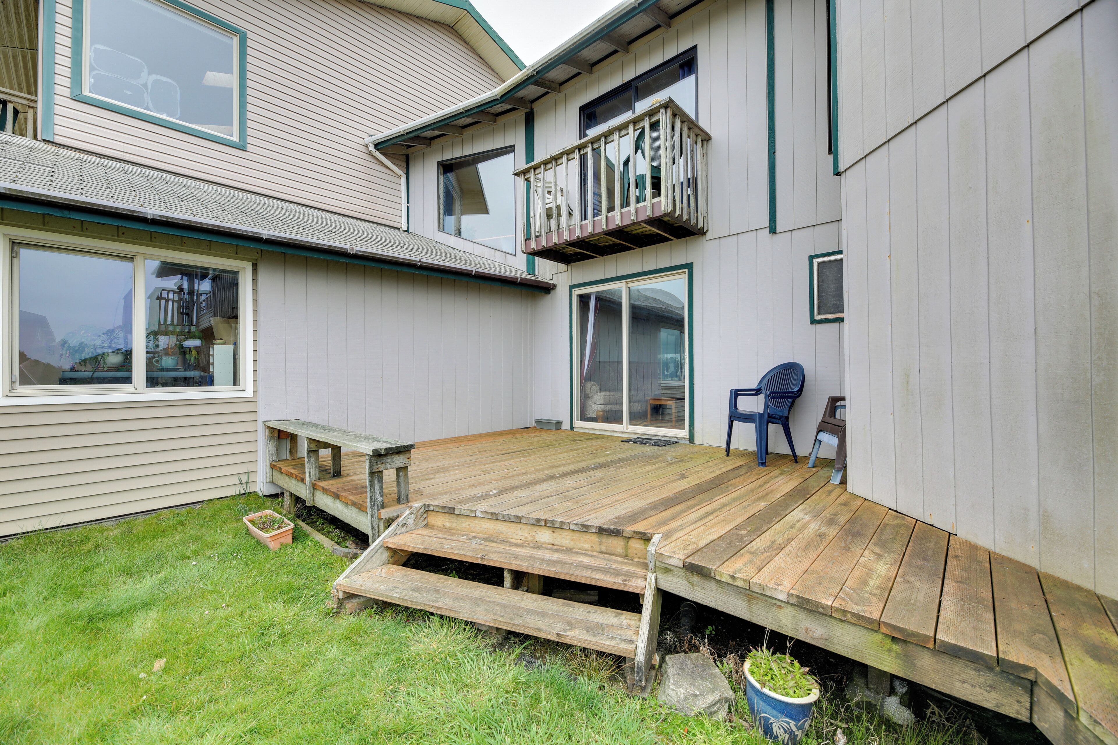 A two-story house with a wooden deck, a small outdoor seating area, and a large window.
