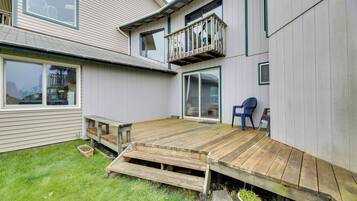 A two-story house with a wooden deck, a small outdoor seating area, and a large window.