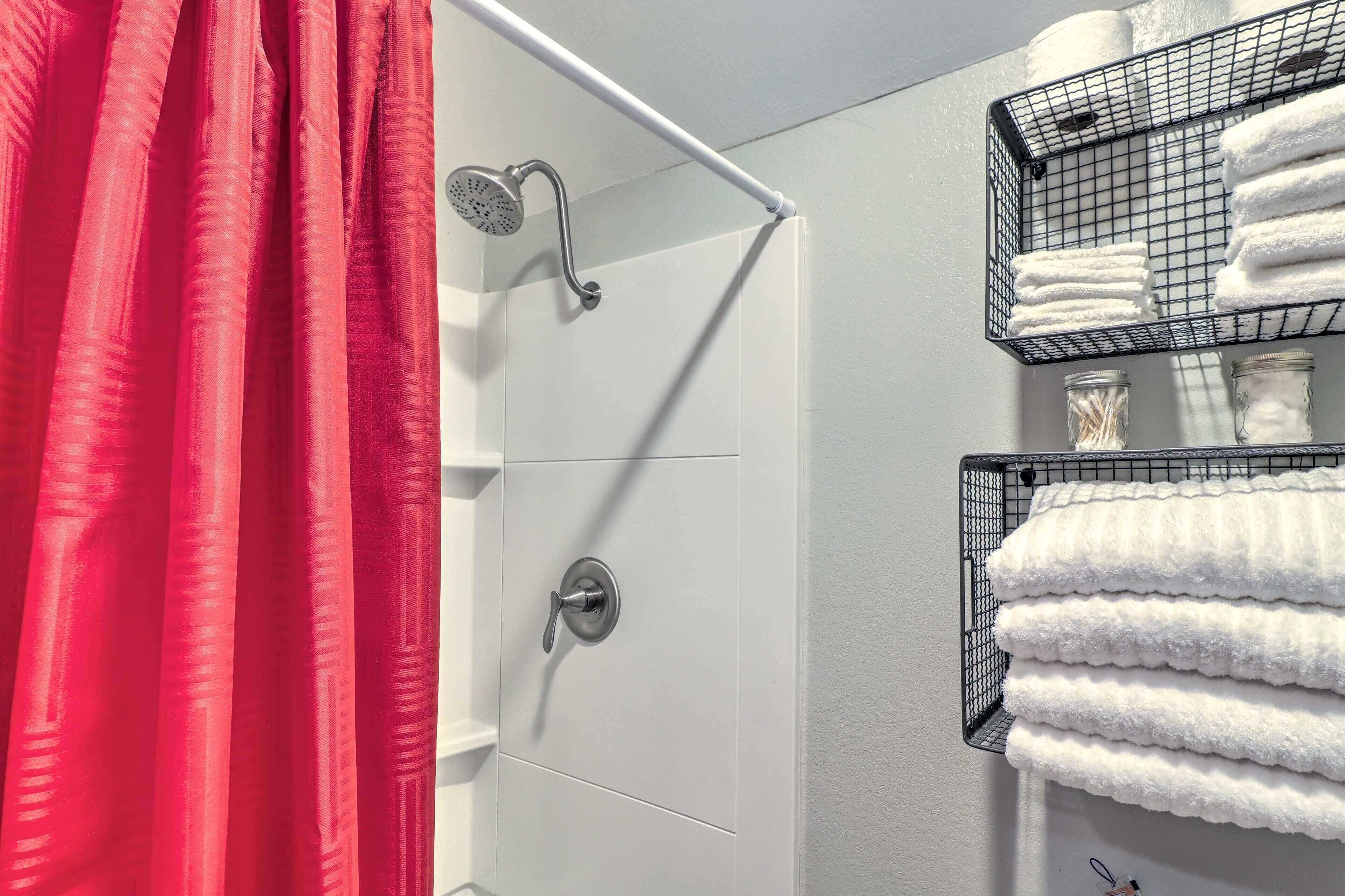 Een badkamer met een douche, een rood gordijn en een rek met netjes opgevouwen handdoeken.