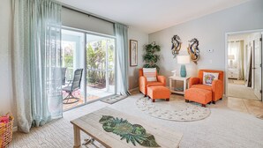 Een woonkamer met een grote schuifpui, twee oranje fauteuils, een houten salontafel en een vloerkleed met een patroon.