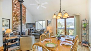 Un salon chaleureux avec une cheminée, un coin repas avec une table en bois dressée pour quatre personnes, et un balcon avec vue.