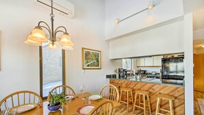 Un espace repas avec des chaises en bois, une table en bois et un coin bar avec des tabourets.
