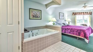 A bathroom with a bathtub, a sink, and a mirror. There is a bed with a green bedspread and a window with curtains. - Cozy Pigeon Condo, Near Lake Huron Beaches! (Pigeon)