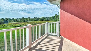A balcony with a red wall, white railing, and a view of a green field and trees. - Cozy Pigeon Condo, Near Lake Huron Beaches! (Pigeon)