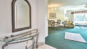 A living room with a glass coffee table, a dining area with chairs, a sofa, and a chandelier. - Cozy Pigeon Condo, Near Lake Huron Beaches! (Pigeon)