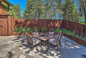 A patio with a wooden table and chairs, surrounded by a wooden fence and trees.