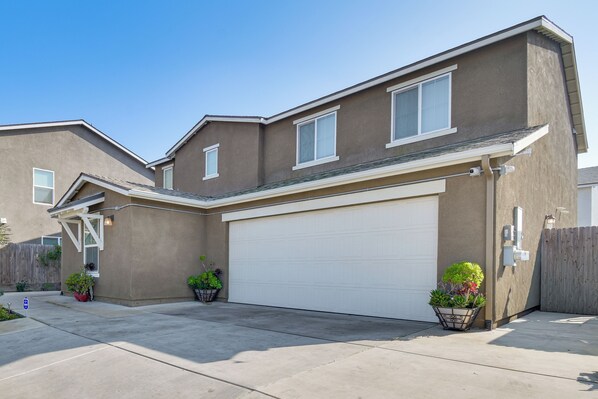 A two-story residential building with a white garage door, a covered entryway, and two potted plants. - Spacious Merced Vacation Rental! (Merced)