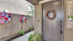 Une entrée d’immeuble d’habitation avec une porte en métal, une pancarte de bienvenue et une clôture en bois ornée de motifs floraux colorés.