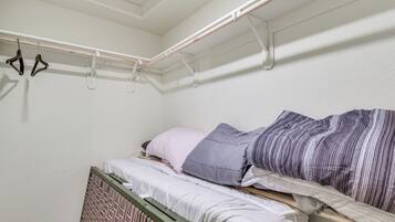 A small, single-bed room with a wooden headboard, a window with a view, and a clothes drying rack with hangers.