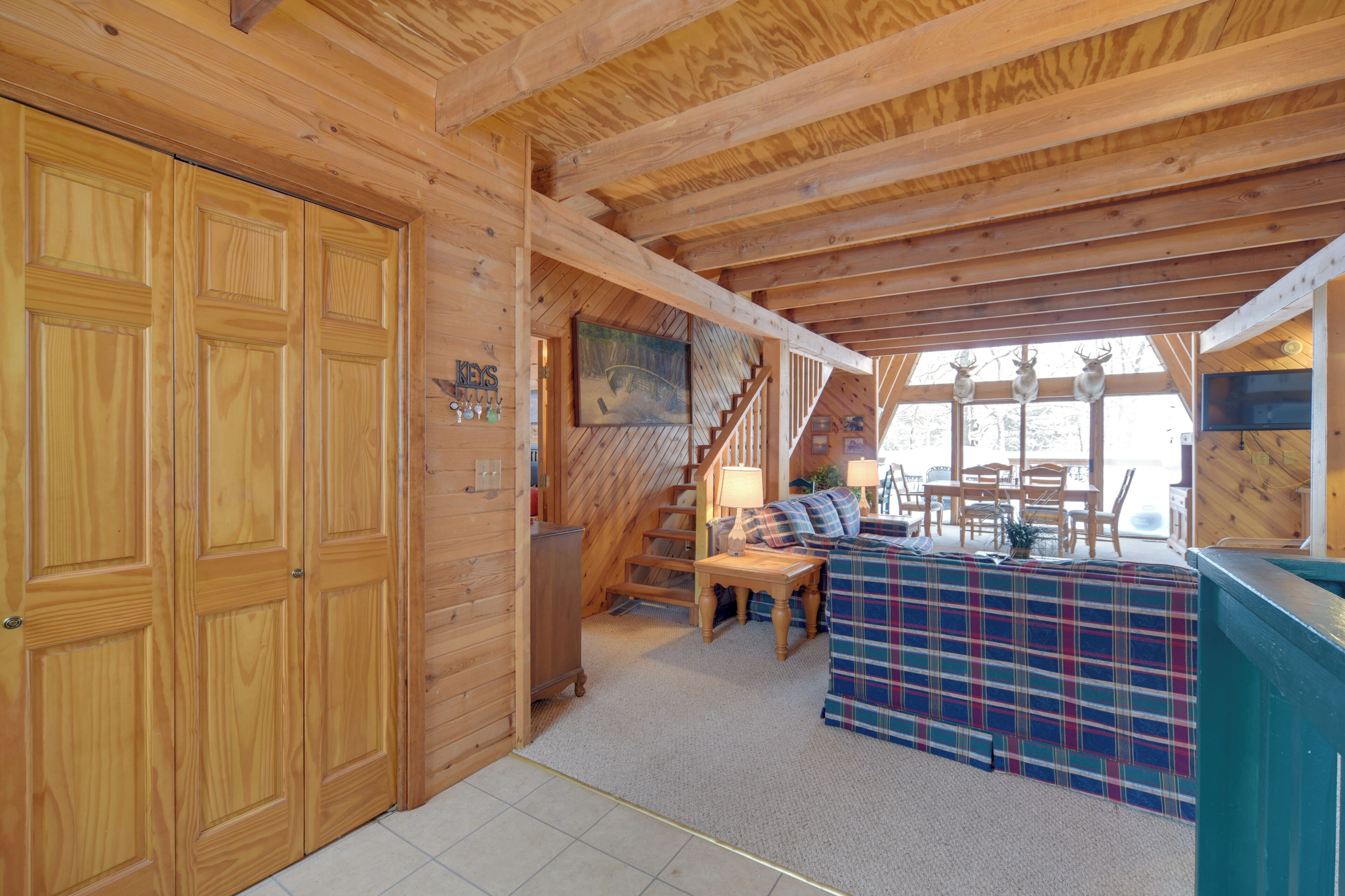 A wooden interior with a staircase, a plaid-covered sofa, and a dining area.