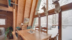 L’intérieur d’un chalet en bois comprend une table à manger, des chaises et deux têtes de cerf fixées sur le cadre de la fenêtre.