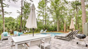 An outdoor patio with a pool, lounge chairs, a table, and umbrellas. - Golf, Dine & Swim: Sleek Palmetto Dunes Home! (Hilton Head Island)